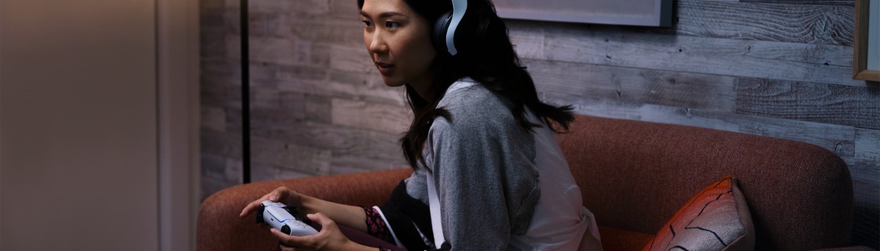  一位女性头戴着耳机，手持Playstation手柄，沉浸在她的娱乐世界中。