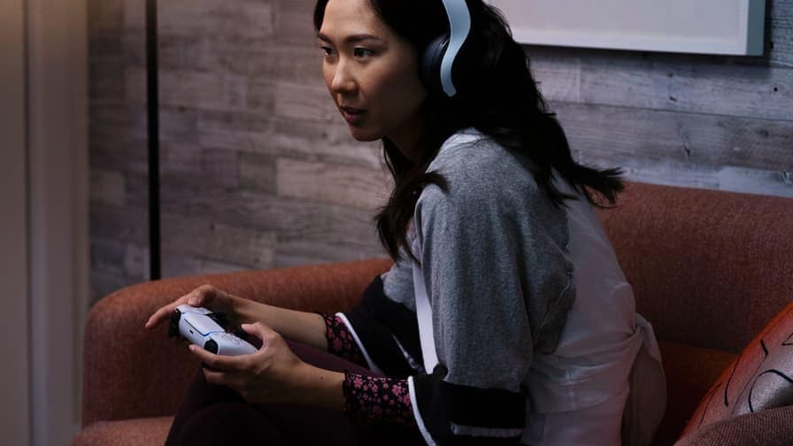  一位女性头戴着耳机，手持Playstation手柄，沉浸在她的娱乐世界中。