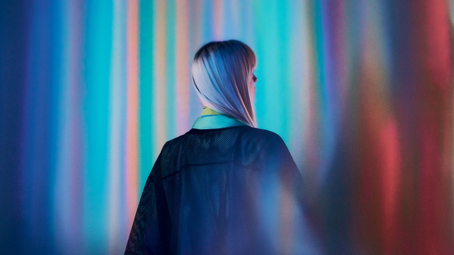 一位穿着黑色连衣裙的女性站在色彩斑斓的背景前，形成鲜明的视觉对比。