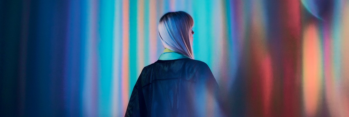 一位穿着黑色连衣裙的女性站在色彩斑斓的背景前，形成鲜明的视觉对比。